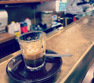 A photo of a short macchiato on the bench of a cafe. 
